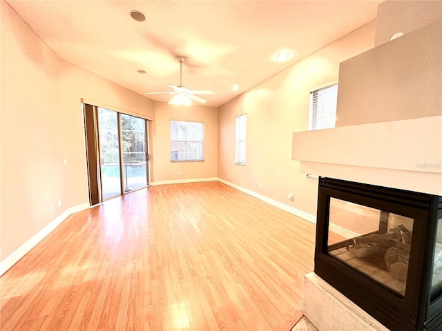 unfurnished living room with baseboards, ceiling fan, light wood finished floors, and a wealth of natural light