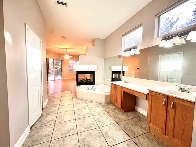 bathroom with tile patterned floors, tiled bath, a multi sided fireplace, vanity, and ceiling fan