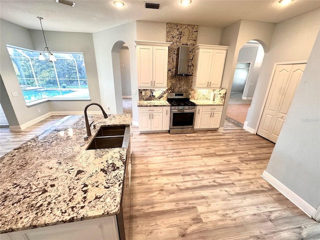 kitchen featuring wall chimney range hood, stainless steel gas range oven, a textured ceiling, a notable chandelier, and sink