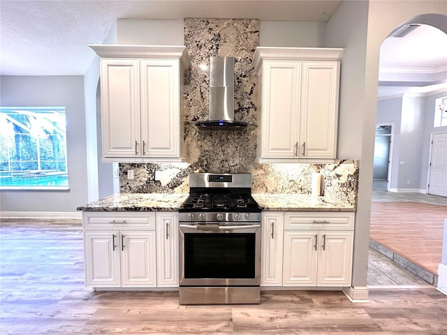 kitchen featuring a wealth of natural light, light hardwood / wood-style flooring, wall chimney range hood, and gas stove