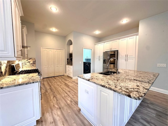 kitchen featuring washer / dryer, light stone countertops, light wood-type flooring, an island with sink, and white cabinets