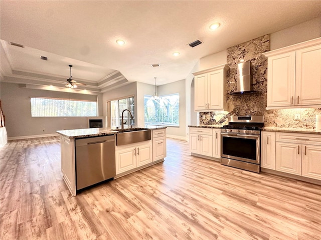 kitchen with wall chimney range hood, light wood-type flooring, sink, pendant lighting, and stainless steel appliances