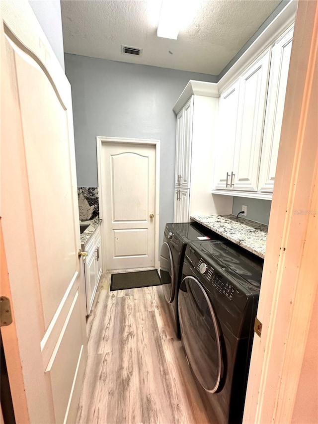 clothes washing area featuring light hardwood / wood-style floors, a textured ceiling, cabinets, and washing machine and clothes dryer