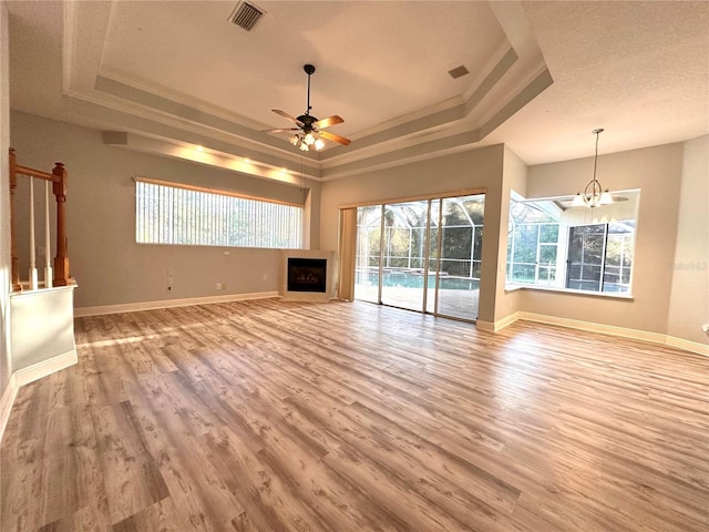 unfurnished living room featuring light hardwood / wood-style flooring, a tray ceiling, crown molding, a textured ceiling, and ceiling fan with notable chandelier