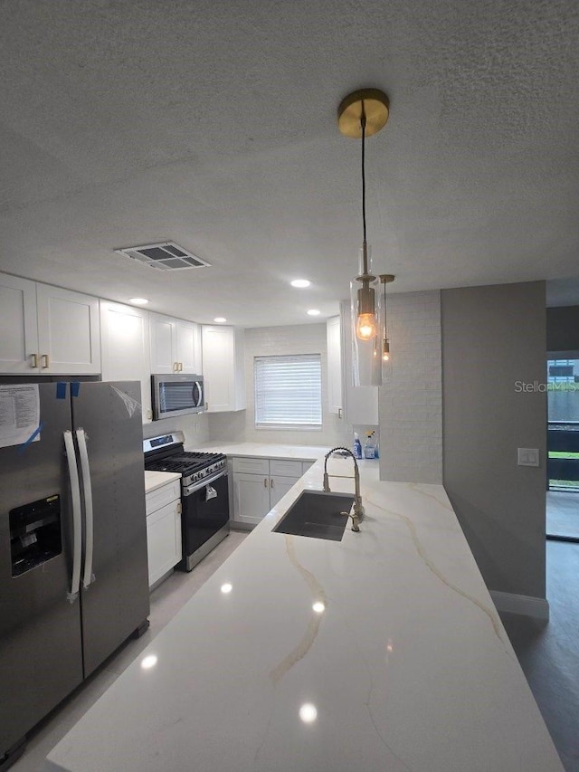 kitchen featuring light stone counters, white cabinetry, stainless steel appliances, sink, and decorative light fixtures