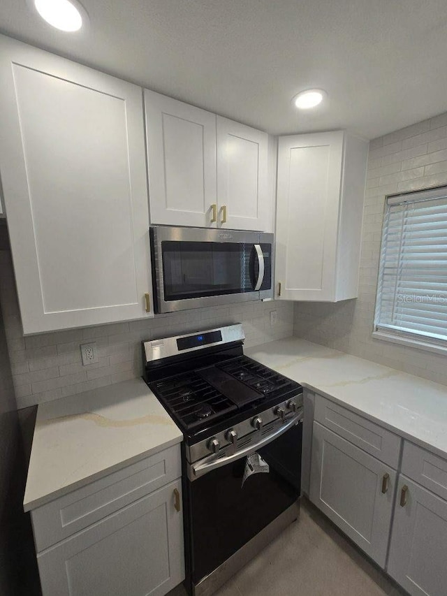 kitchen with light stone counters, stainless steel appliances, decorative backsplash, and white cabinets