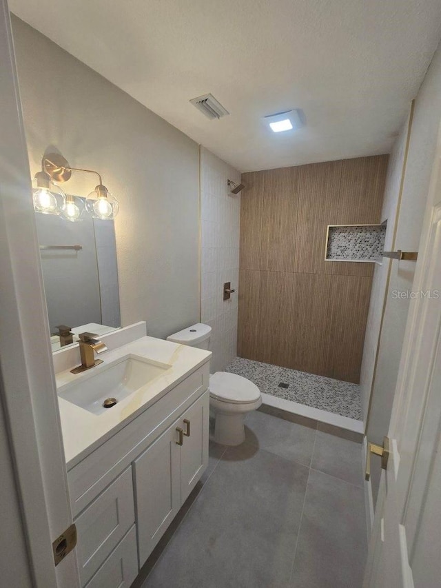 bathroom featuring toilet, vanity, tile patterned floors, and tiled shower