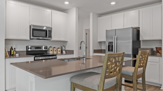 kitchen with white cabinets, a center island with sink, appliances with stainless steel finishes, hardwood / wood-style flooring, and sink