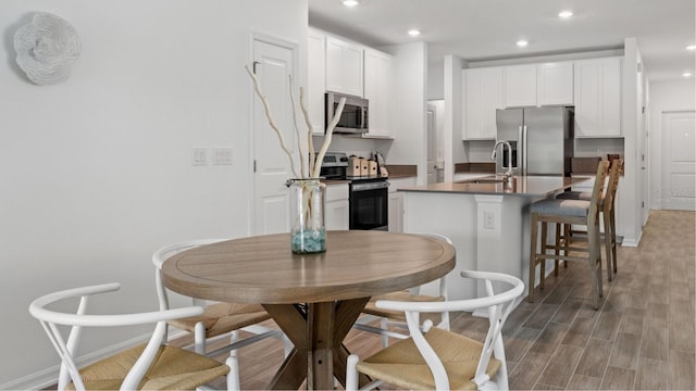 kitchen with light hardwood / wood-style flooring, white cabinets, stainless steel appliances, and a kitchen bar