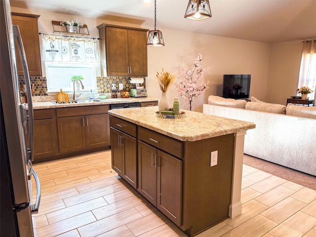 kitchen with hanging light fixtures, sink, a center island, light wood-type flooring, and stainless steel refrigerator