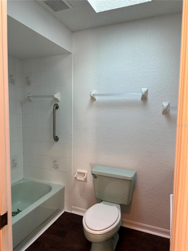 bathroom with toilet, hardwood / wood-style floors, tiled shower / bath combo, a textured ceiling, and a skylight