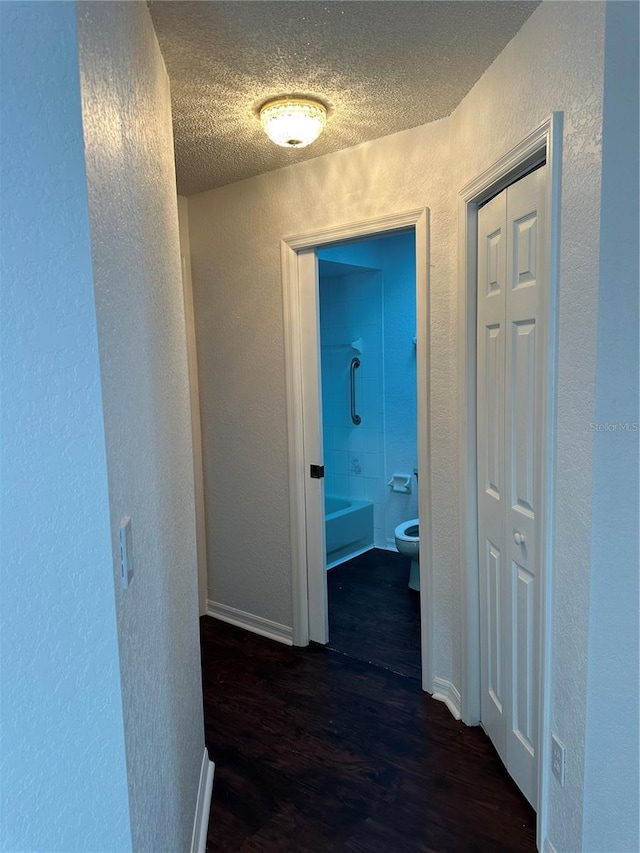 hallway with a textured ceiling and dark hardwood / wood-style floors