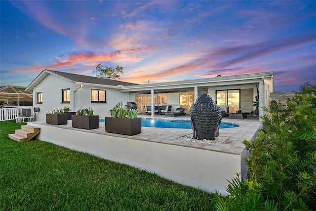 back house at dusk featuring outdoor lounge area, a yard, and a patio