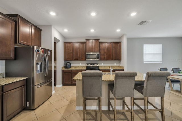 kitchen with a breakfast bar, appliances with stainless steel finishes, light stone counters, and a kitchen island with sink