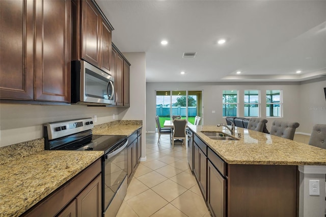 kitchen with a wealth of natural light, sink, stainless steel appliances, light stone counters, and a kitchen island with sink