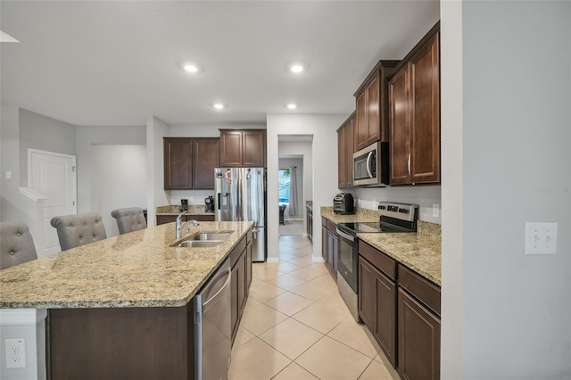 kitchen with appliances with stainless steel finishes, light stone counters, a kitchen island with sink, and sink