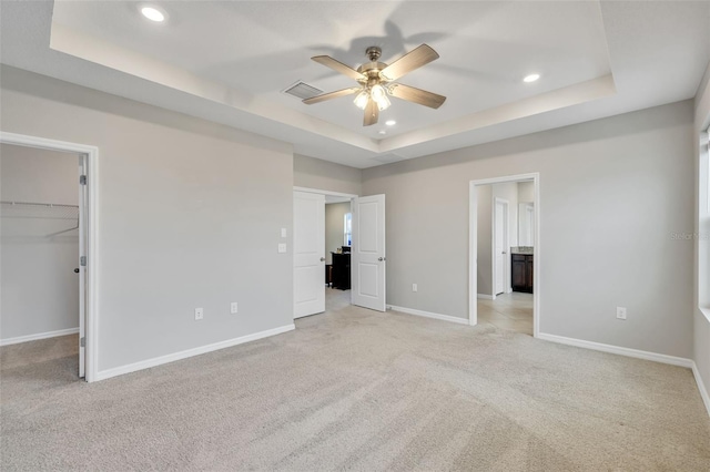 unfurnished bedroom featuring a raised ceiling, a spacious closet, ceiling fan, and light colored carpet