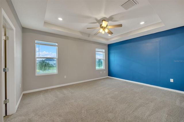 carpeted empty room with a raised ceiling and ceiling fan