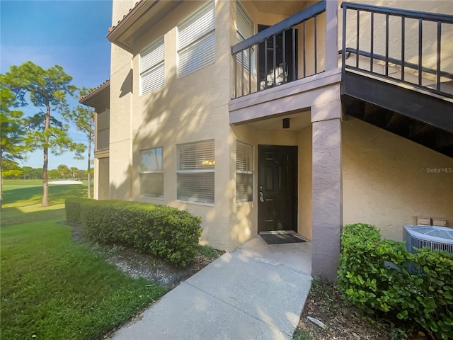 view of exterior entry with central air condition unit, a lawn, and a balcony