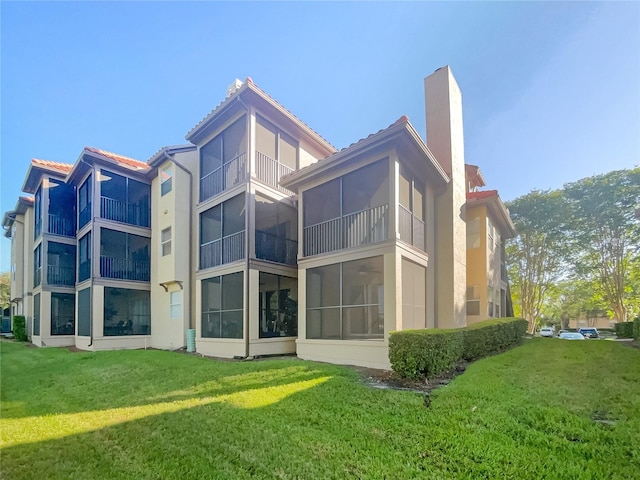 back of house with a sunroom, a lawn, and a balcony