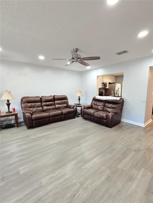 living room featuring light hardwood / wood-style floors, a textured ceiling, and ceiling fan