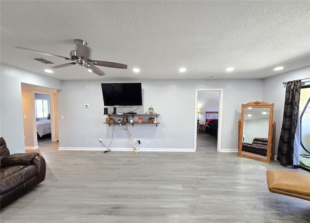 living room with ceiling fan, a textured ceiling, and light hardwood / wood-style floors