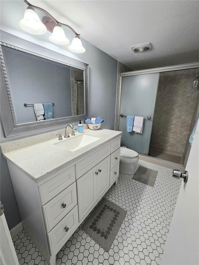 bathroom featuring toilet, tile patterned floors, a shower with shower door, and vanity