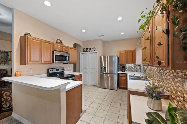 kitchen with kitchen peninsula, backsplash, appliances with stainless steel finishes, light tile patterned flooring, and sink