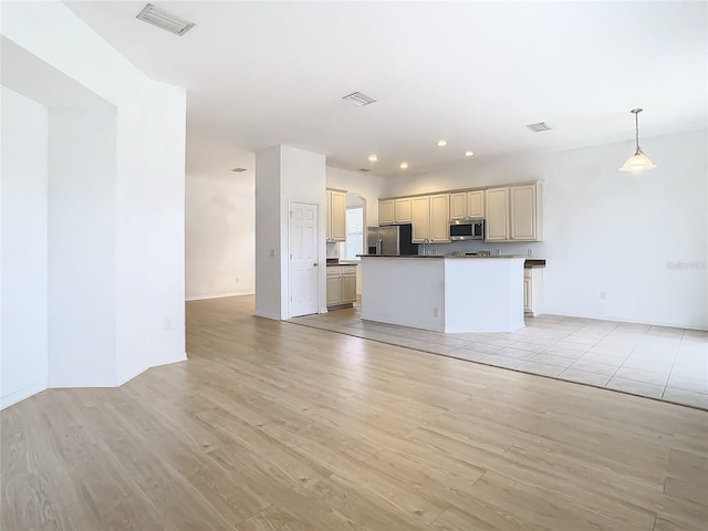 kitchen featuring cream cabinets, a center island, decorative light fixtures, light hardwood / wood-style flooring, and stainless steel appliances