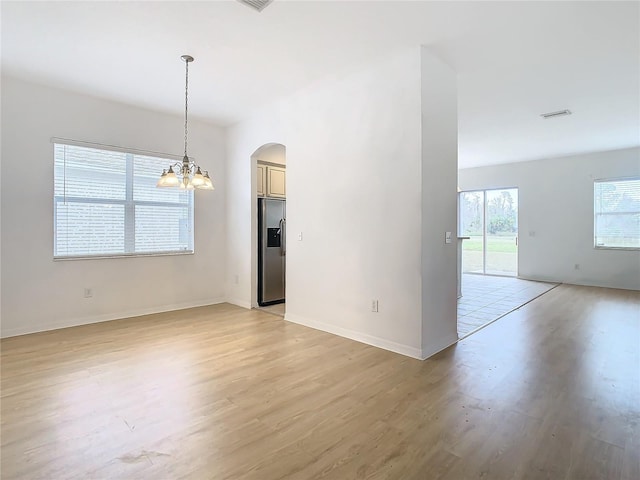 empty room with light hardwood / wood-style floors and an inviting chandelier