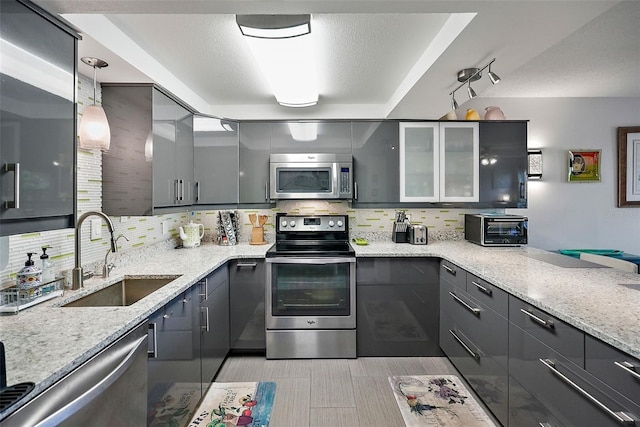 kitchen with stainless steel appliances, sink, decorative light fixtures, and light stone countertops