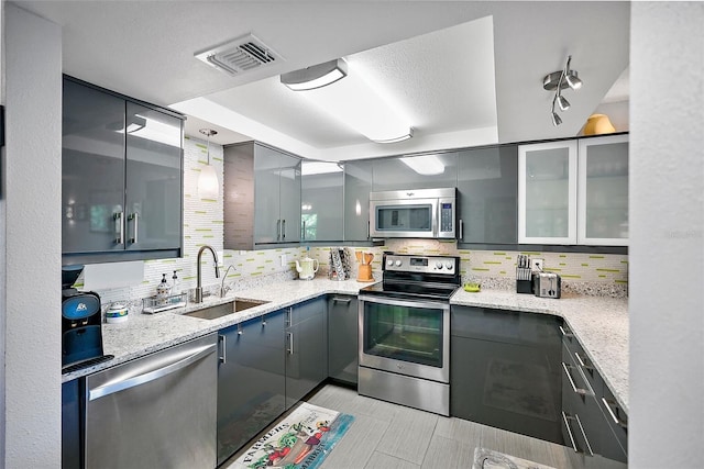 kitchen with light stone counters, sink, tasteful backsplash, gray cabinetry, and appliances with stainless steel finishes