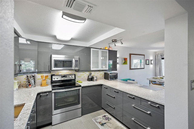 kitchen featuring kitchen peninsula, appliances with stainless steel finishes, gray cabinetry, and light stone countertops