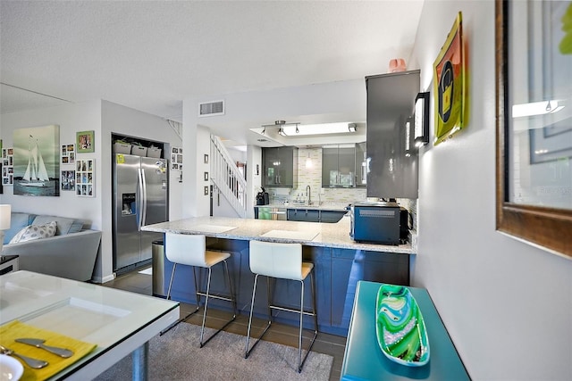 kitchen with sink, a breakfast bar, kitchen peninsula, stainless steel fridge with ice dispenser, and decorative backsplash