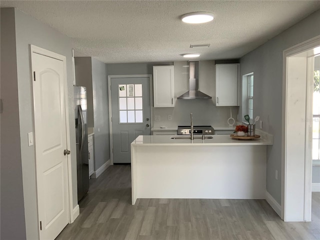 kitchen with wall chimney exhaust hood, white cabinetry, hardwood / wood-style floors, and kitchen peninsula