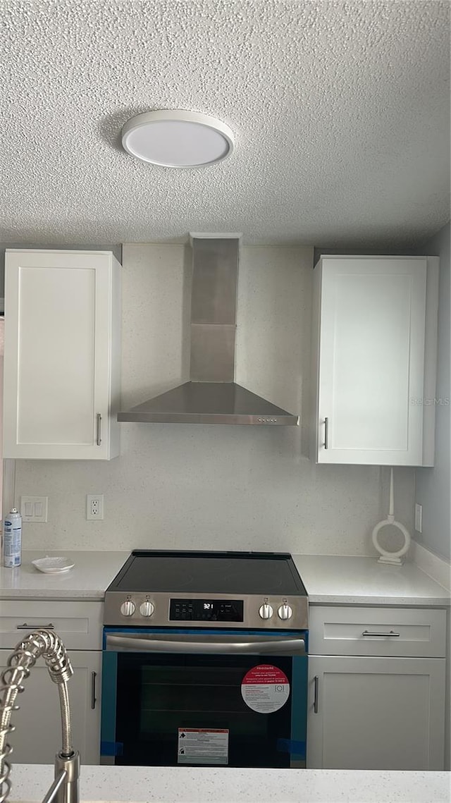 kitchen with white cabinetry, stainless steel range with electric stovetop, wall chimney range hood, and a textured ceiling