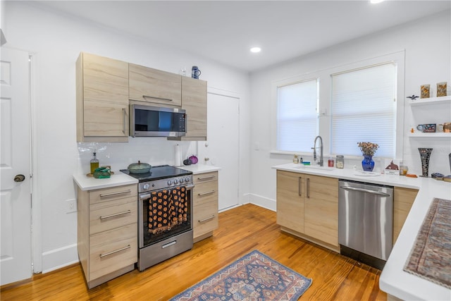 kitchen with appliances with stainless steel finishes, sink, light brown cabinetry, and light hardwood / wood-style floors