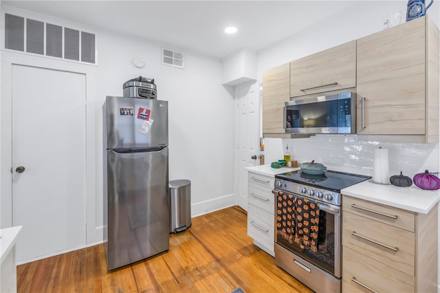 kitchen featuring light brown cabinetry, tasteful backsplash, appliances with stainless steel finishes, and light wood-type flooring