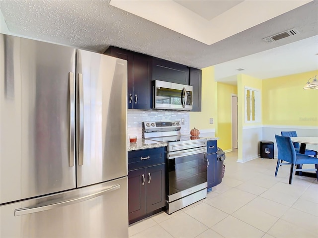 kitchen featuring decorative backsplash, light stone counters, stainless steel appliances, and a textured ceiling