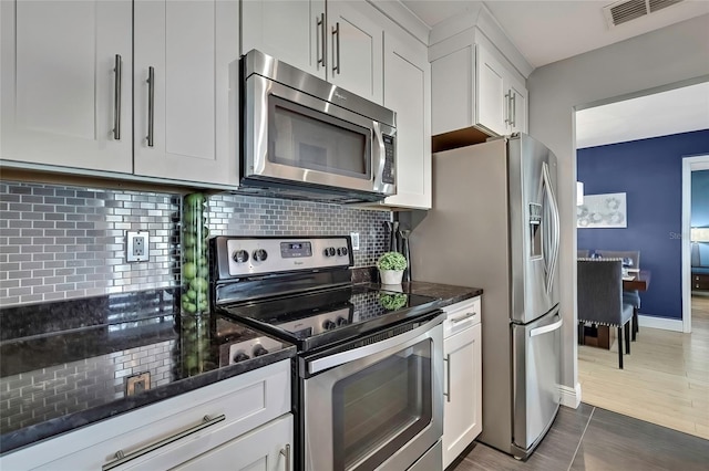 kitchen with tasteful backsplash, stainless steel appliances, dark tile patterned floors, dark stone countertops, and white cabinetry