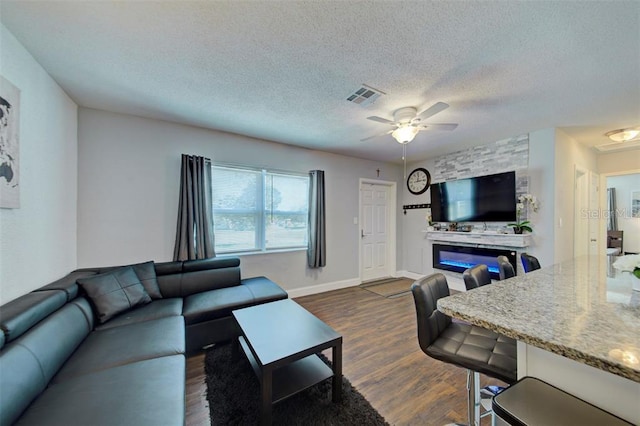 living room featuring a textured ceiling, a fireplace, dark hardwood / wood-style floors, and ceiling fan