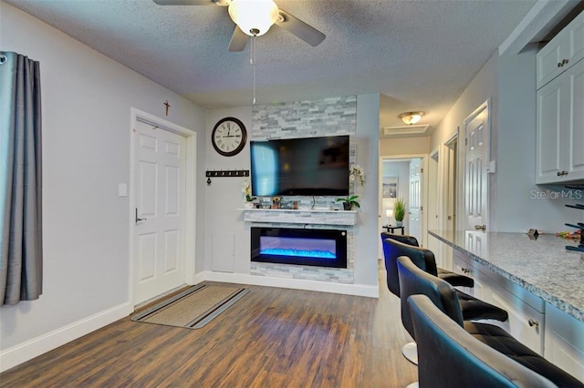 living room with dark wood-type flooring, a large fireplace, a textured ceiling, and ceiling fan