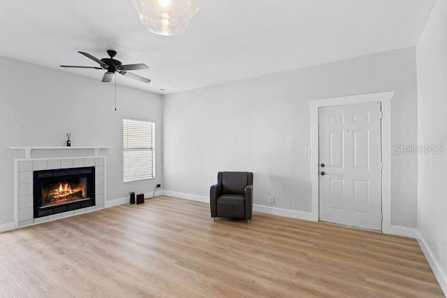 unfurnished room featuring light hardwood / wood-style flooring, a tiled fireplace, and ceiling fan