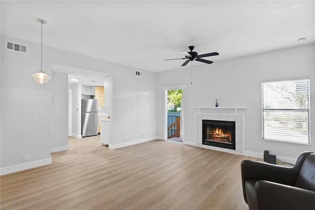 living room featuring a tile fireplace, light wood-type flooring, and ceiling fan