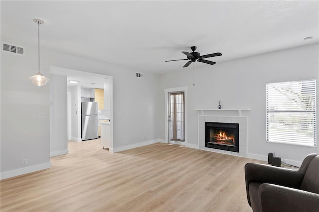 living room with light hardwood / wood-style flooring, a tiled fireplace, and ceiling fan