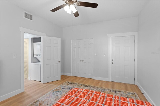 bedroom featuring stacked washer and clothes dryer, light wood-type flooring, and ceiling fan