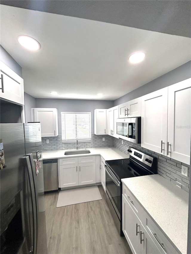 kitchen featuring light hardwood / wood-style flooring, stainless steel appliances, sink, white cabinets, and tasteful backsplash