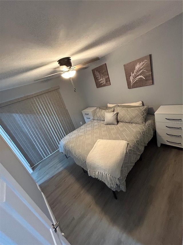 bedroom with a textured ceiling, dark wood-type flooring, and ceiling fan