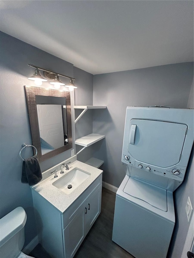 bathroom with toilet, hardwood / wood-style floors, stacked washer / dryer, and vanity