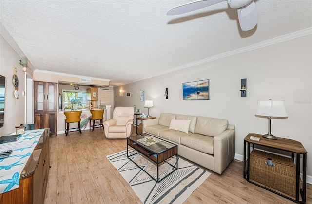 living room with ceiling fan, ornamental molding, a textured ceiling, and light wood-type flooring